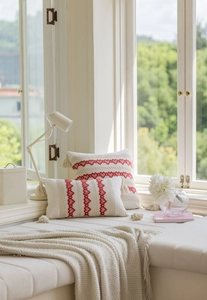Detail of cream jacquard pillows with red hearts and decorative pom-poms on a window sill