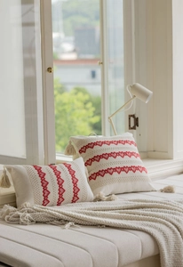 Detail of jacquard pillows with red heart embroidery and tassels on a cozy window seat