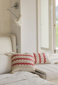 Close-up of cream throw pillow with red embroidered heart pattern and corner tassels