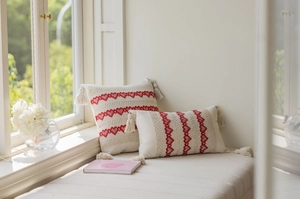 Close-up of red heart embroidery and corner tassels on a cream boho throw pillow