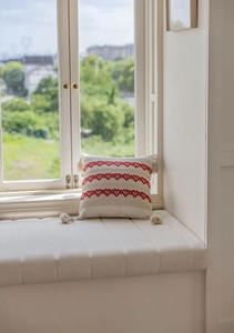 Detail of red heart embroidery and corner tassels on a cream jacquard throw pillow