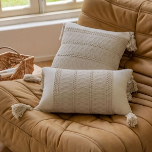 Boho style beige textured sofa pillows with tassels on a dark brown leather couch