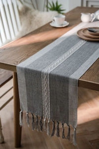 Close-up of gray woven table runner with white wave embroidery and handcrafted tassels