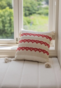 Detail of red heart embroidery and corner tassels on a cream textured throw pillow