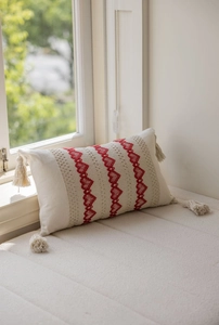 Detail view of a beige lumbar pillow featuring red heart embroidery and tassels on corners