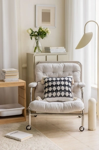 Detail of a geometric black and white throw pillow with tassels on a beige armchair
