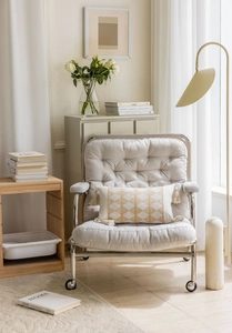 Detail of beige armchair with silver casters and a yellow geometric pattern tassel pillow