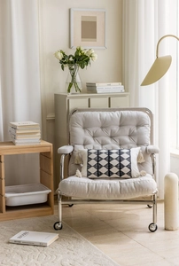Detail of modern armchair featuring cream fabric with black geometric tufted pillow and tassels