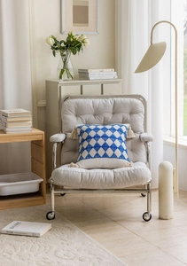 Detail of blue geometric jacquard pillow with white tassels on a grey lounge chair
