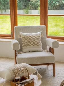 Nahaufnahme von beigem Jacquard-Kissen mit geometrischem Häkelmuster und Quasten auf Stuhl