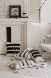 Detail of four black and white woven pillow covers with tassels in a cozy home setting