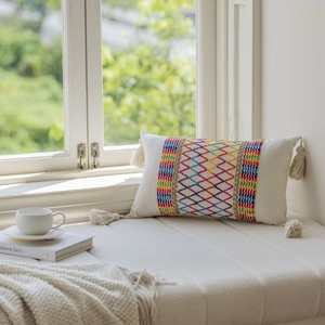 Rectangular boho pillow with colorful diamond embroidery and fringe details by window
