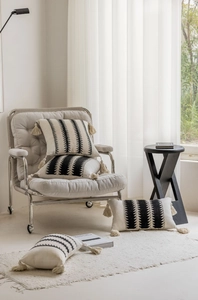Bohemian woven pillow with black geometric patterns and handmade tassels on soft armchair