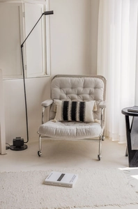 Detailed view of black and white striped tassel pillow on a quilted light grey armchair