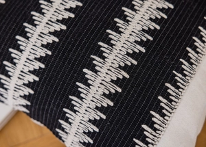 Detail of black cotton fabric with white wavy hand embroidery and heavy texture