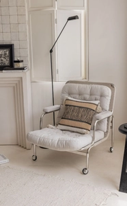 Detail of modern armchair with chrome frame, soft white cushion, and striped tassel pillow