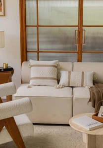 Detail of woven jacquard pillow cover with tassels on a minimalist beige fabric sofa