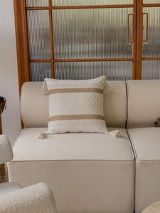 Detail of cream jacquard throw pillow with tassel accents and woven texture on a sofa