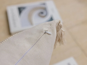 Close-up of invisible zipper and woven tassel fringe on beige linen sofa pillow cover