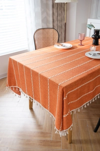 Détail d'une nappe en coton lin orange avec rayures géométriques et pompons blancs