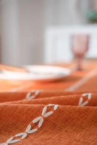 Gros plan détaillé de la nappe en lin orange avec motifs de broderie papillon blancs