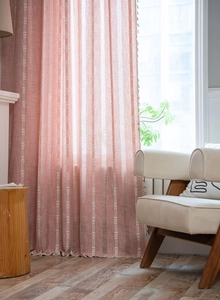 Détail de rideaux corail semi-transparents avec rayures verticales et pompons décoratifs