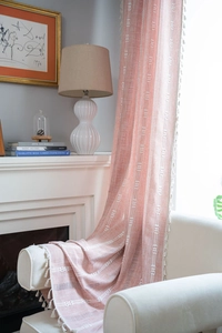 Détail d'un rideau tissé orange corail avec broderie géométrique blanche et franges