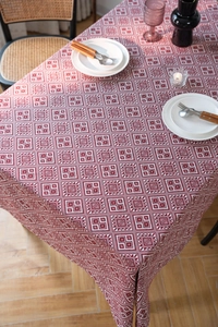 Detailed view of red jacquard tablecloth with white geometric diamond patterns on a wood table