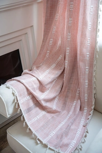 Détail du tissu de rideau orange clair avec broderie géométrique blanche et franges