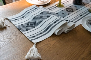 Dettaglio di un runner da tavola intrecciato con motivi geometrici e nappe