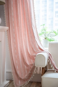 Détail de rideau rayé rose corail en coton et lin avec des bordures de franges à glands