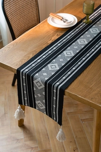 Close-up of bohemian table runner featuring geometric diamond patterns and cotton tassels