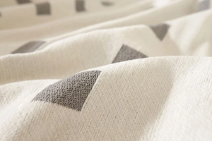 Close-up of thick woven fabric with gray geometric triangles on a cream tablecloth
