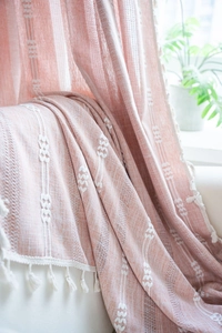 Détail de jeté de canapé en tricot rose avec broderie géométrique et pompons blancs