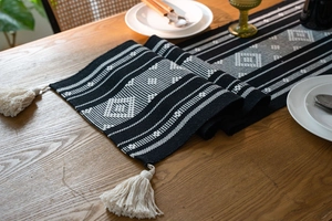 Close-up of geometric jacquard table runner with white tassels on a wooden dining table