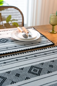 Dettaglio di tovagliette boho in bianco e nero con motivi geometrici e finiture a nappa