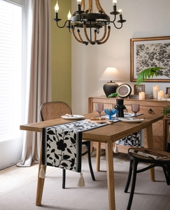 Detail of jacquard table runner with black floral patterns and off-white fringe tassels