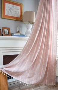Détail d'un rideau rose corail avec des motifs de vagues blanches et des franges à glands
