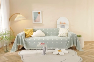 Detailed view of light green knit sofa cover with white jacquard pattern and fringe tassels
