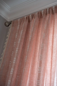 Gros plan de rideaux rose corail avec motifs géométriques blancs et bords à glands