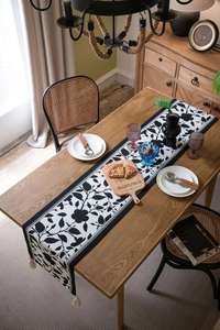 Detail of floral jacquard table runner with black and white patterns and white tassels