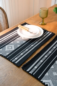 Detail view of woven cotton placemats with black and white geometric patterns on a wood table