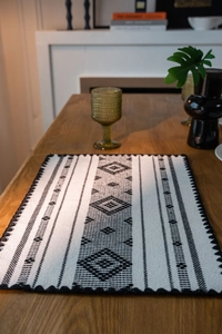 Dettaglio di un runner da tavola in cotone con motivi geometrici neri e nappe boho