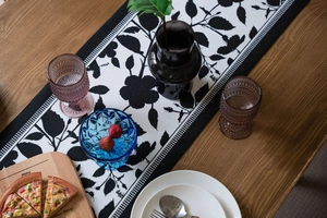 Detail view of jacquard table runner featuring black leaf patterns on a wooden table
