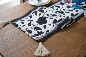 Detailed view of jacquard floral table runner with cream tassels on a wooden dining table
