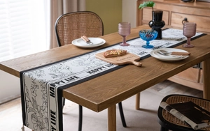 Macro detail of black and white floral jacquard table runner with HAPPY LIFE fringe