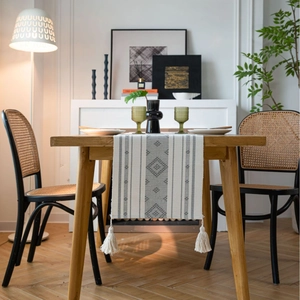 Runner da tavola bohémien con motivi geometrici e nappe su tavolo in legno