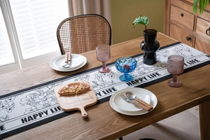 Detailed close-up of a black and white floral table runner with Happy Life slogan on wood