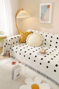 Detail of a thick minimalist beige sofa throw featuring black geometric grid and tassels