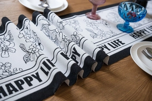 Detail of jacquard table runner featuring black and white floral sketches and Happy Life text
